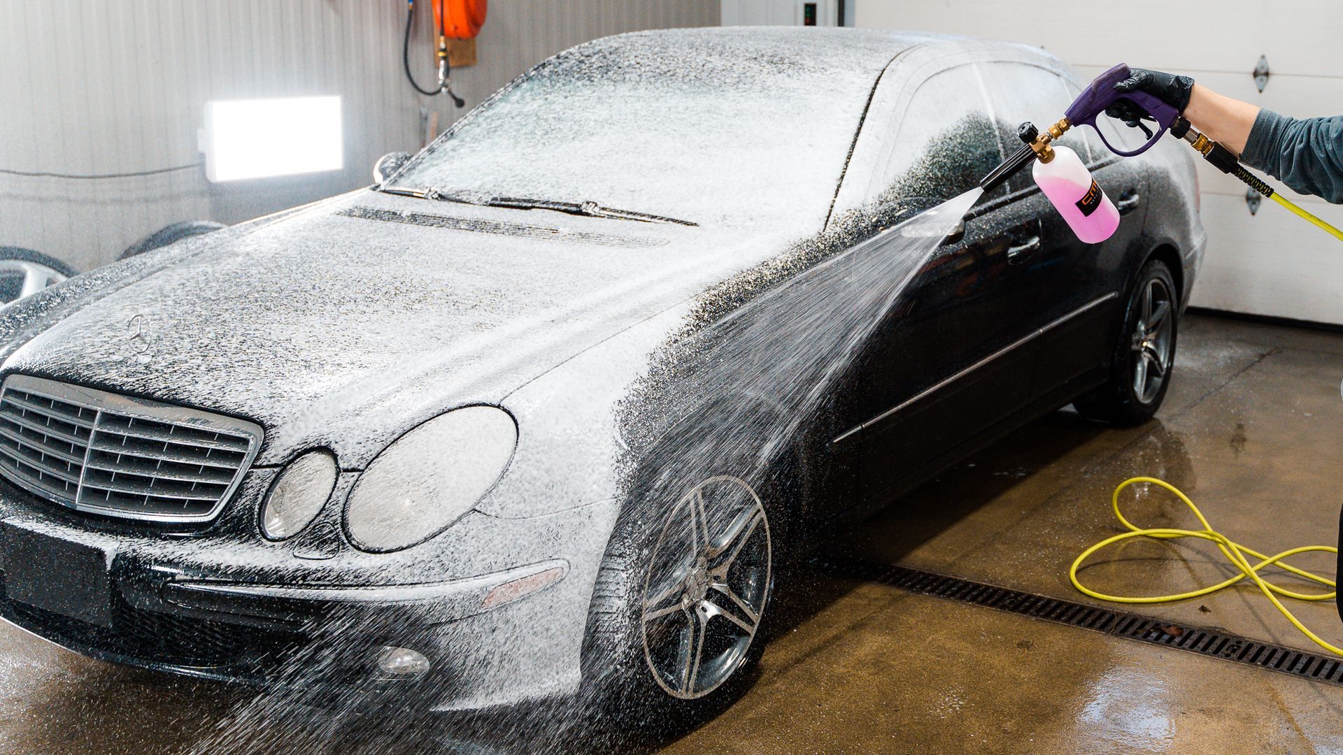 Person washing a shiny black SUV with a blue hose; indoors, bright lighting.