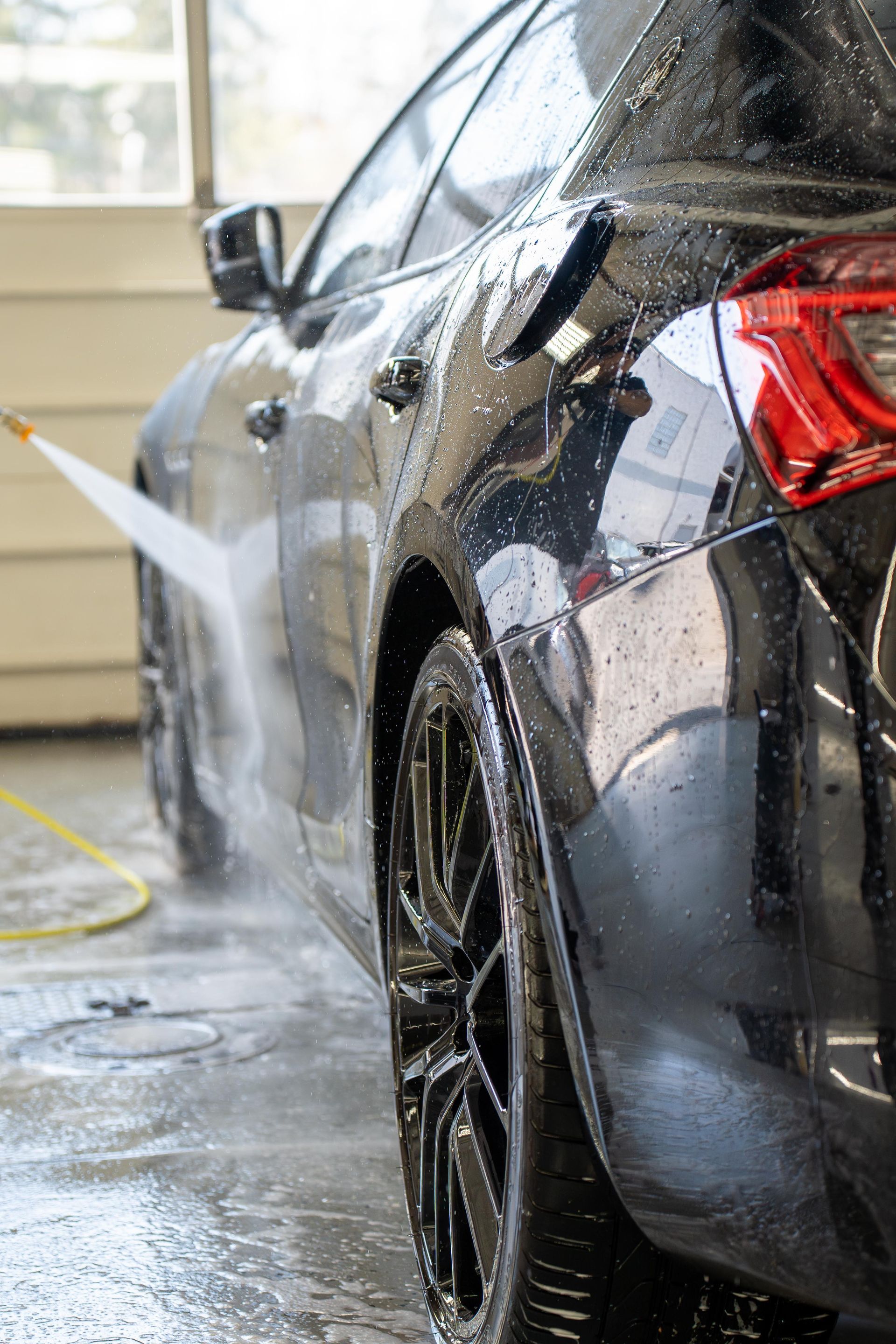 Black car being washed with a pressure washer, water spraying on the side and tire.