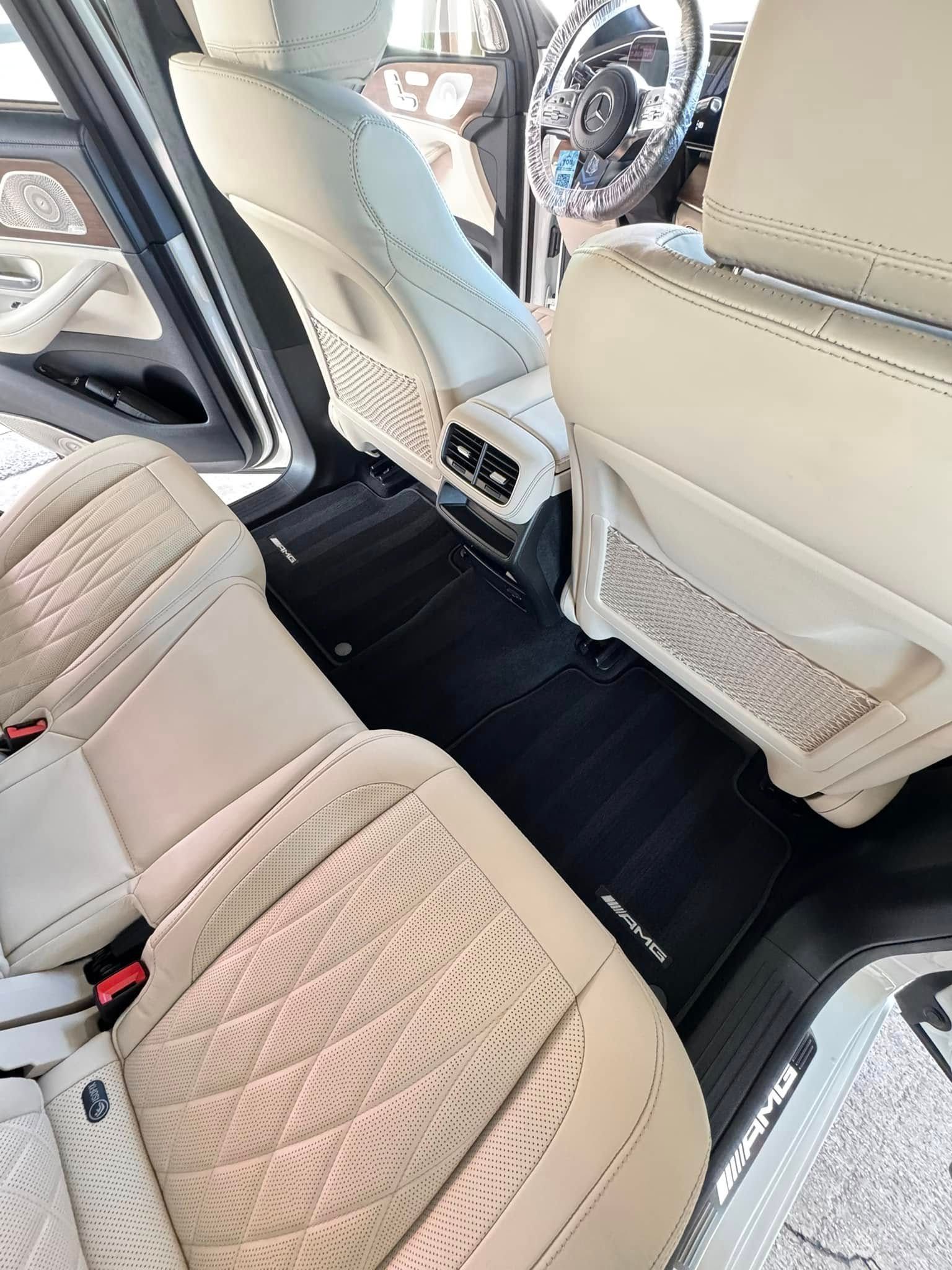 Interior view of a light-colored car with leather seats, black floor mats, and a chrome steering wheel.