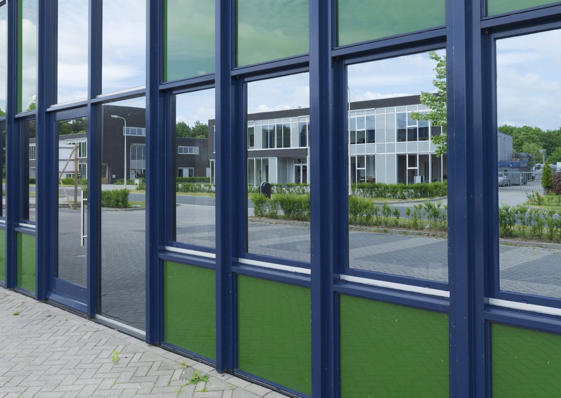 Blue and green building facade with large windows reflecting surrounding buildings.