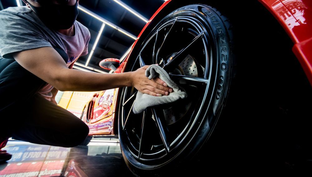 Person wearing a mask cleaning a shiny black car wheel with a cloth.
