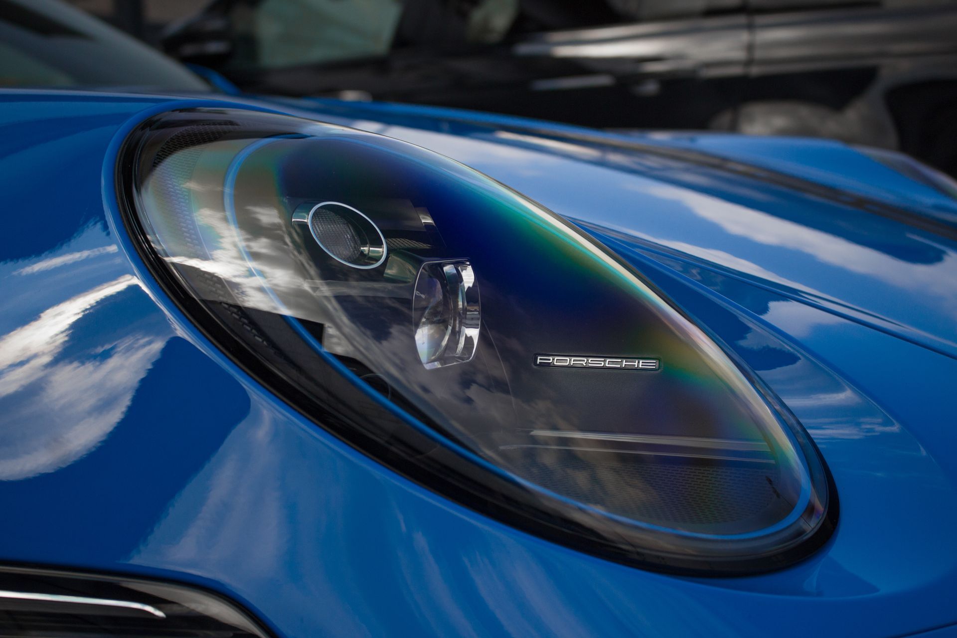 Blue car headlight with a reflection of sky and other cars.