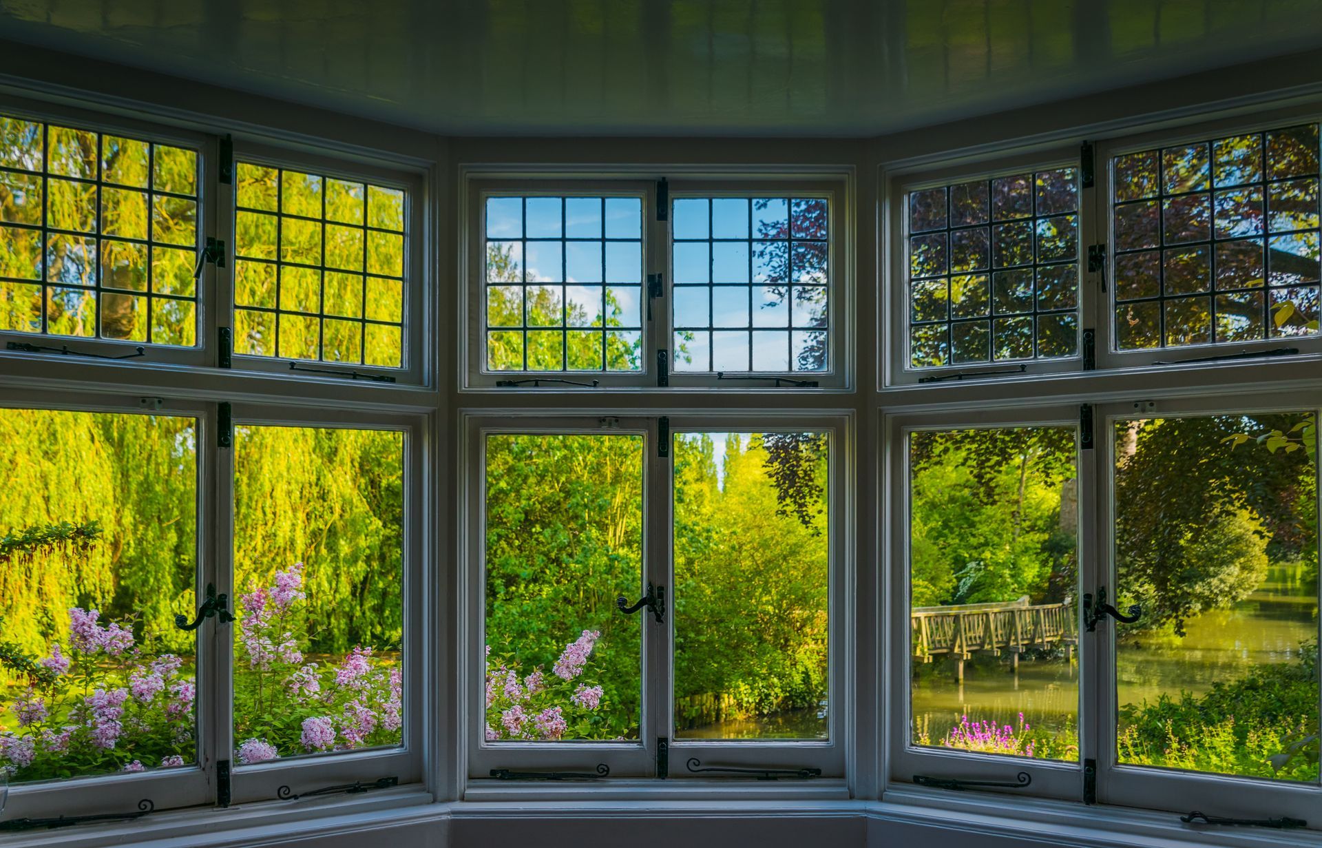 Bay window with white trim framing a view of lush green trees, a body of water, and blue sky.