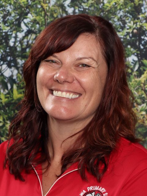 Woman with curly blonde hair and black headband smiles in a red shirt against a green backdrop.