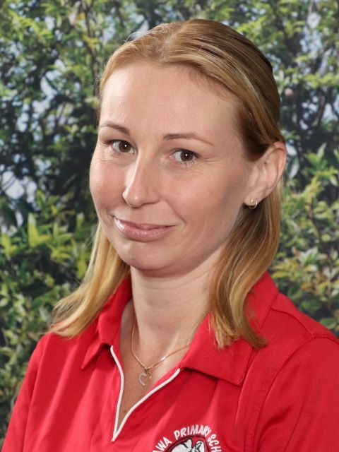 Smiling young woman with brown hair in a red collared shirt, outdoors.