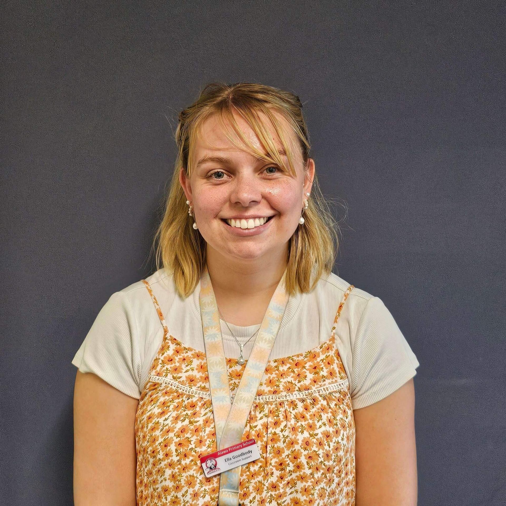 Person with long dark hair, smiling, wearing a red polo shirt, against a blurred leafy background.