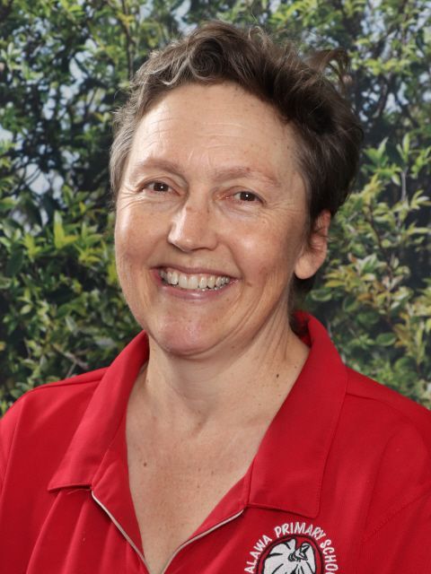 Woman with long dark hair smiling, wearing a red shirt against a green leafy background.