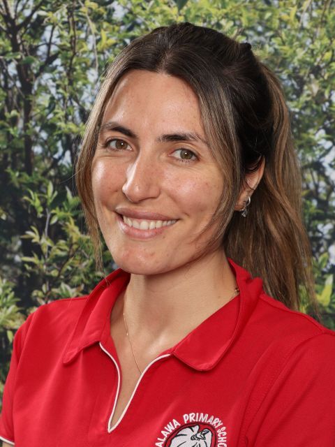 Woman smiling in red polo shirt, set against greenery.