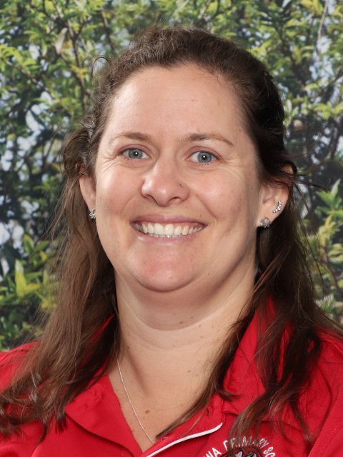 Woman with blonde hair wearing a red polo shirt smiling; outdoor background.