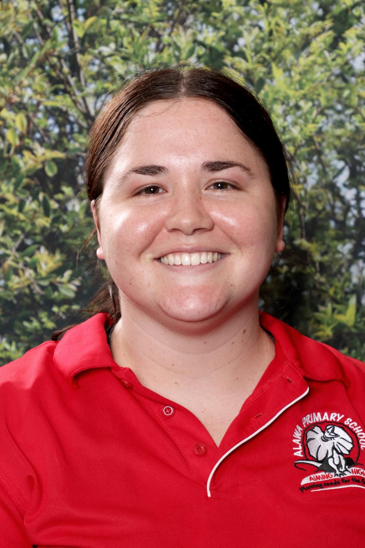 Woman with curly blonde hair wearing a red polo shirt and black headband smiles at the camera.