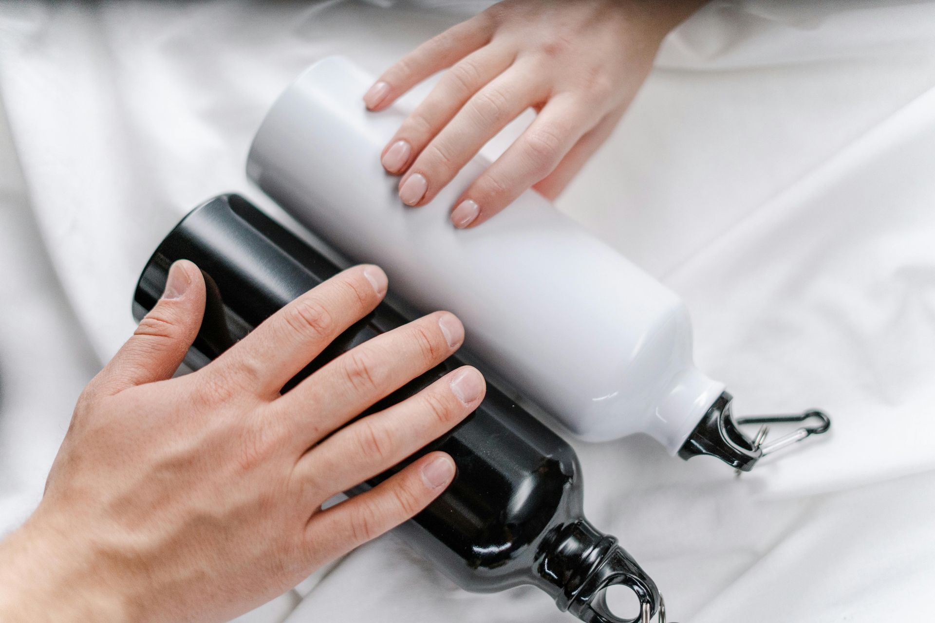 Hands holding a black and a white water bottle on white fabric.