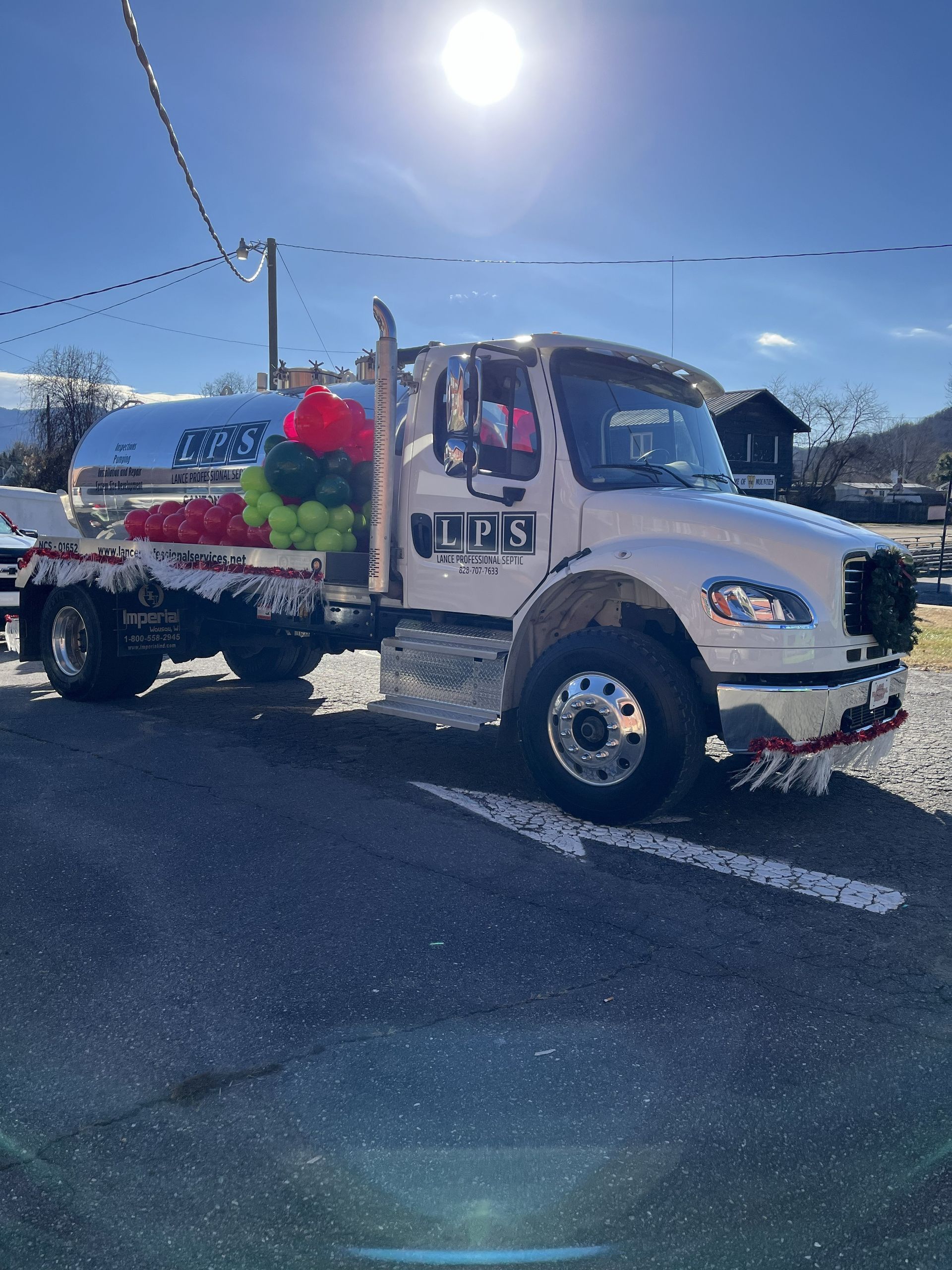White tow truck with colorful holiday decorations parked in bright sunlight on a snowy street