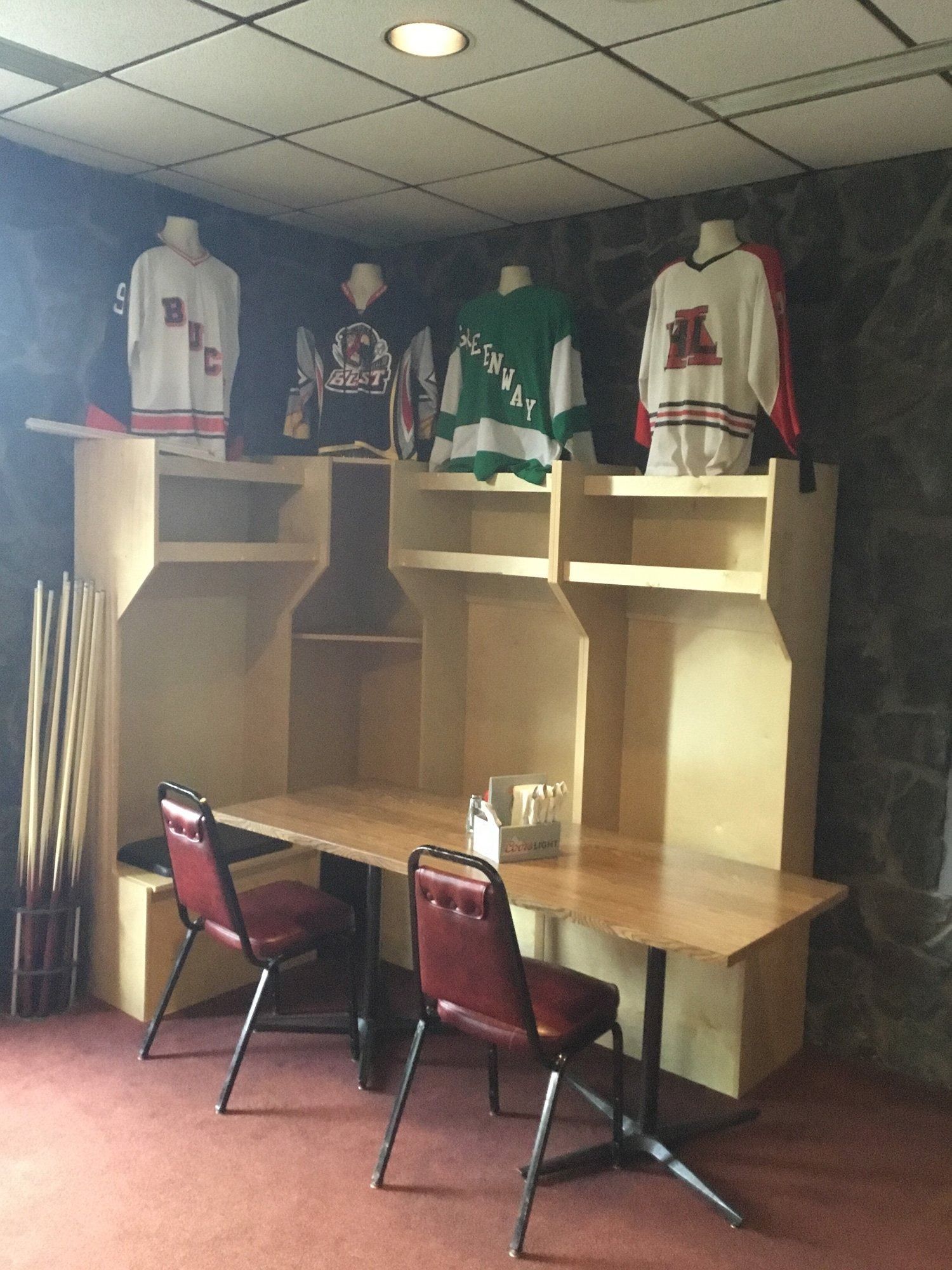 Small room with wooden desk, two red chairs, and sports jerseys displayed on shelves.