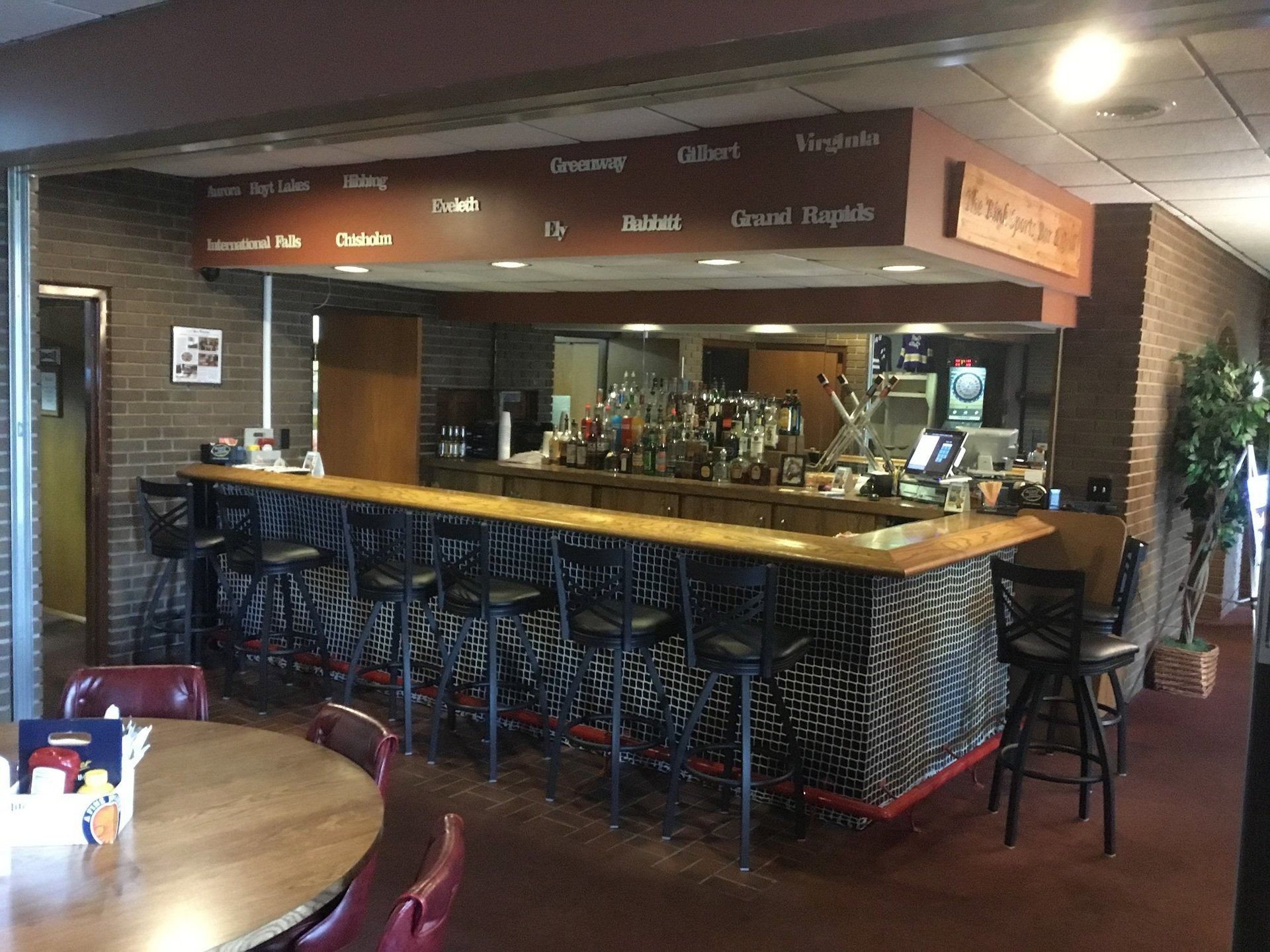 Empty sports bar with a long wooden counter, high stools, and a TV in the background
