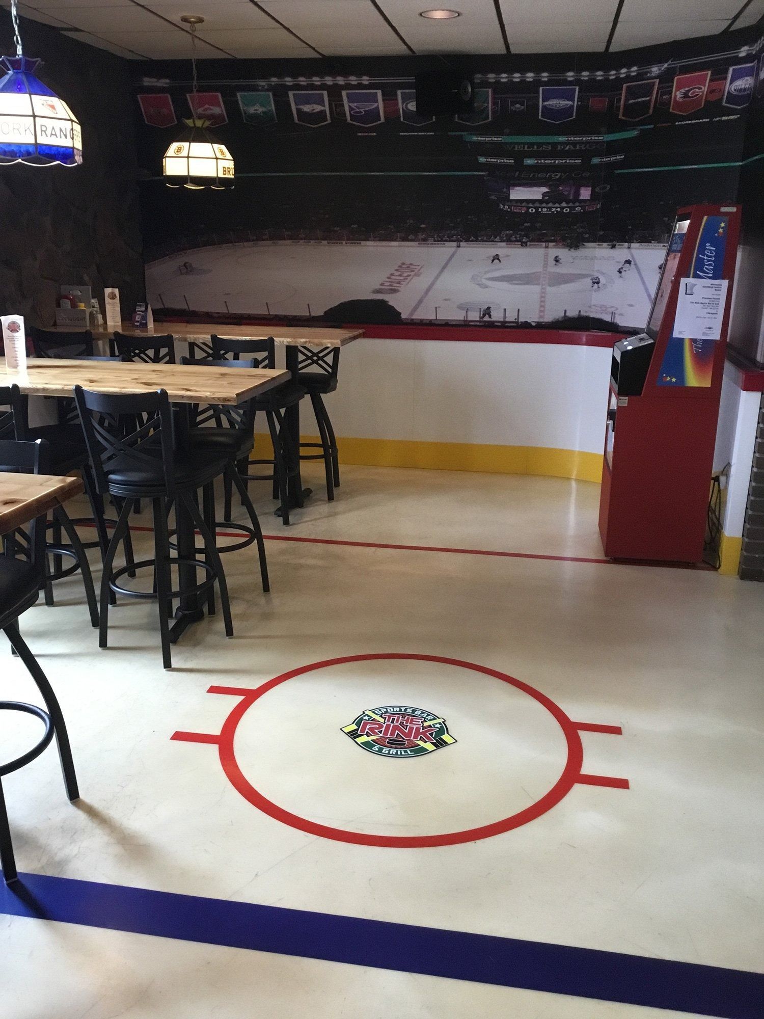 Empty sports-themed restaurant interior with rink-style floor markings and hanging lights