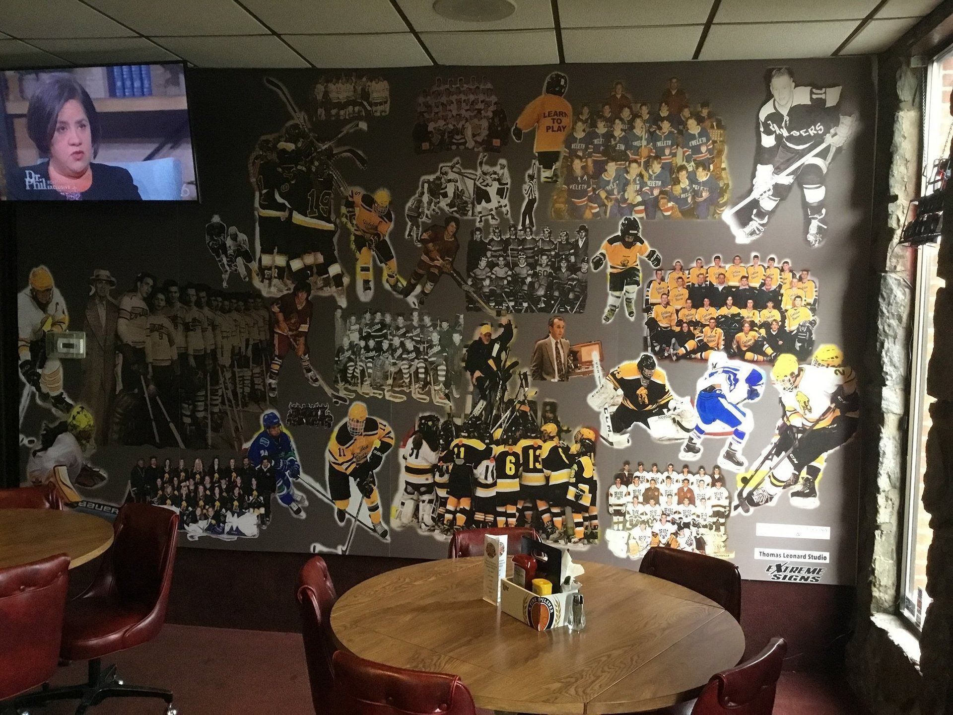 Dim sports-themed room with a collage wall, TV in corner, and round wooden table with chairs.