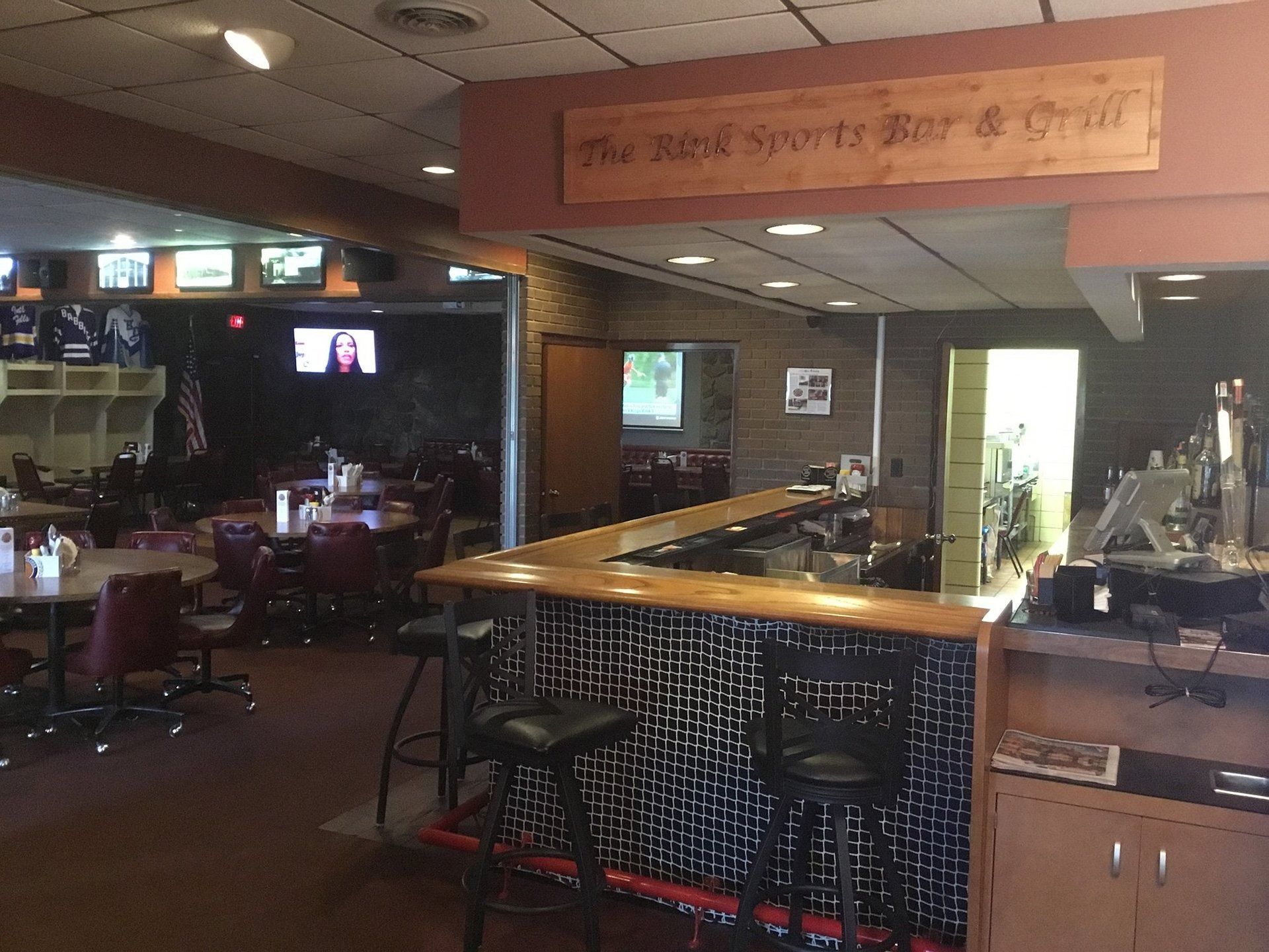 Dimly lit bar interior with wooden counter, stools, TV screens, and a pool table in the background