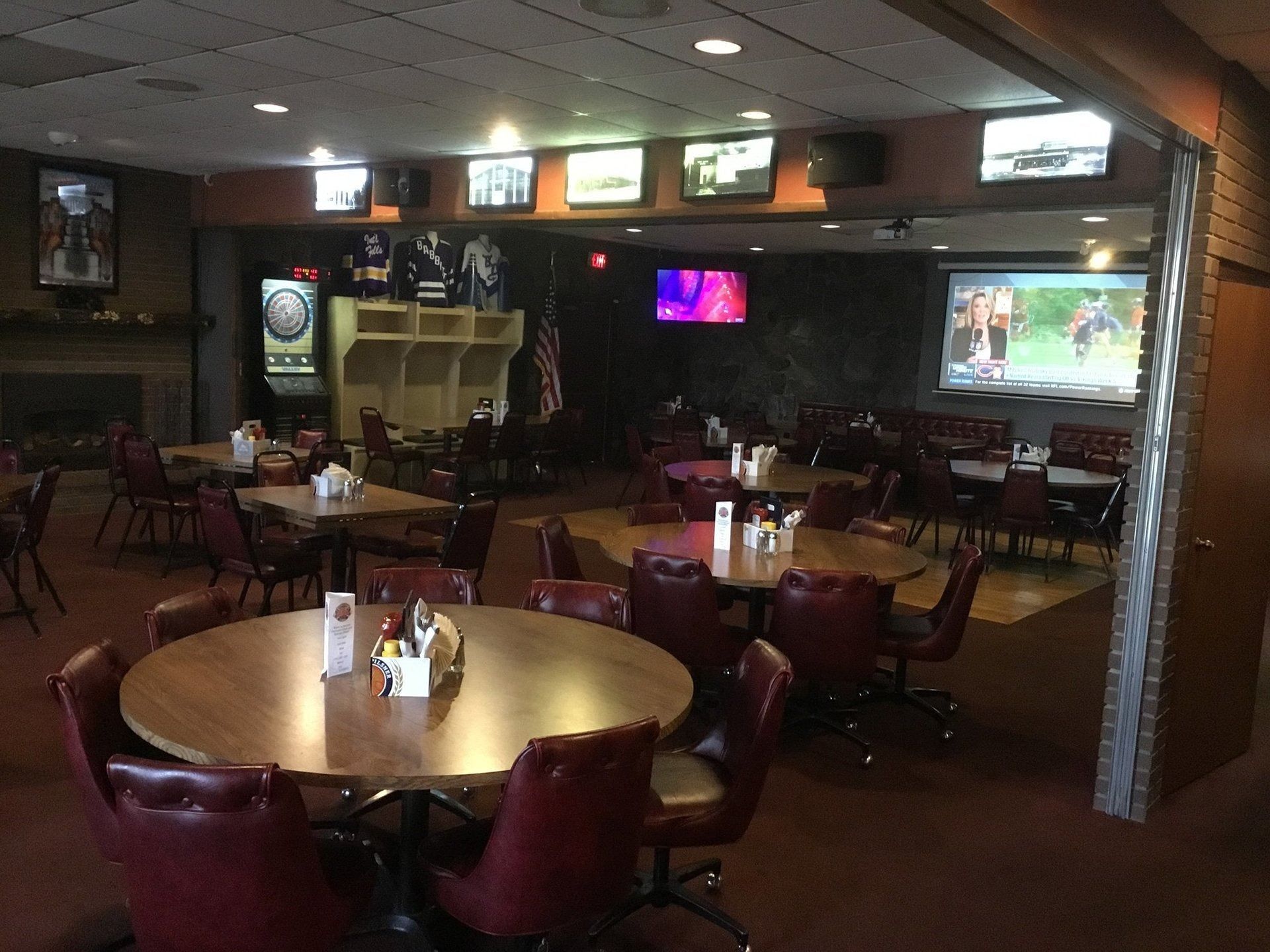 Empty sports bar with round tables, red booths, and TVs showing a game.