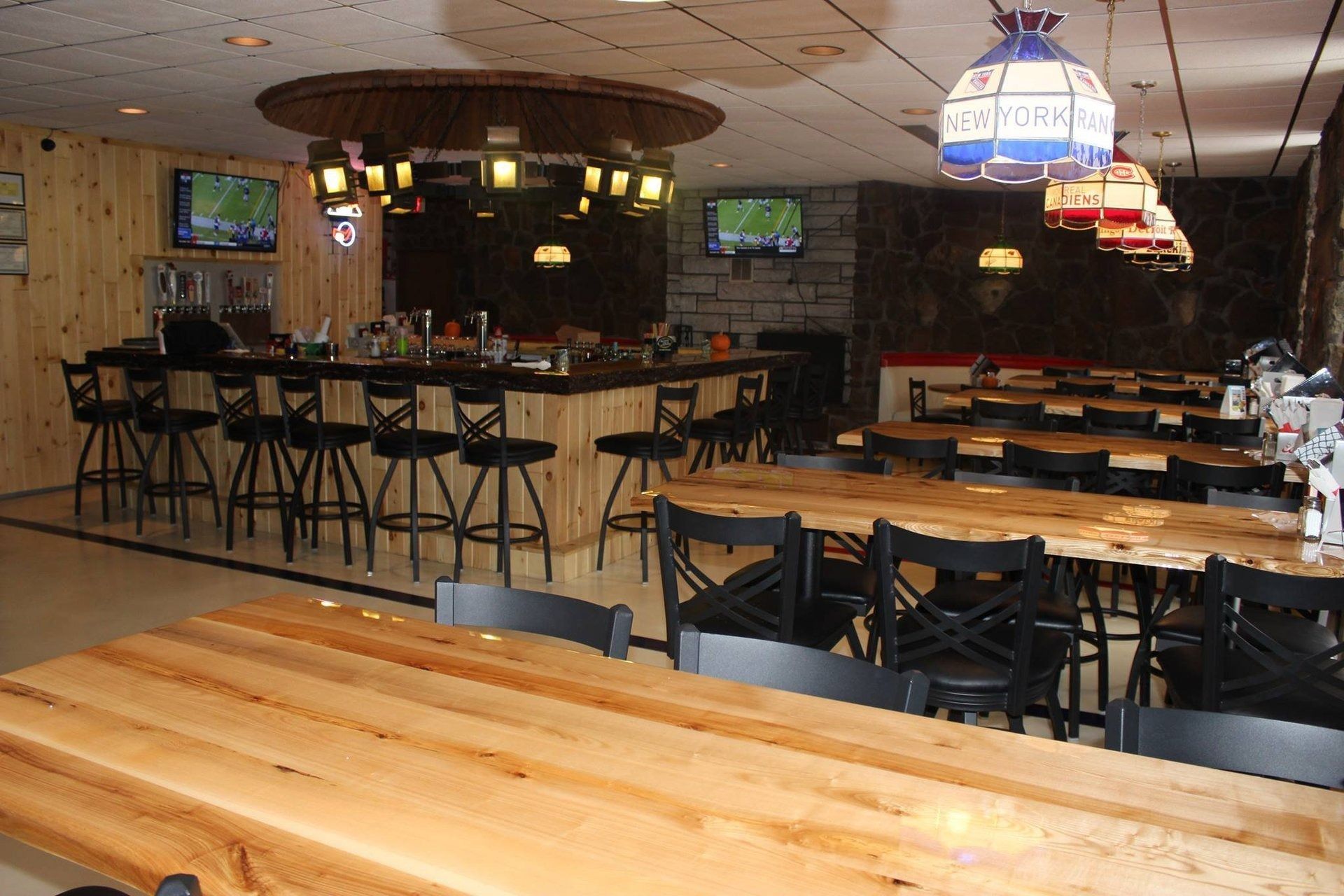 Empty bar interior with wooden tables, high stools, and TV screens under dim lighting