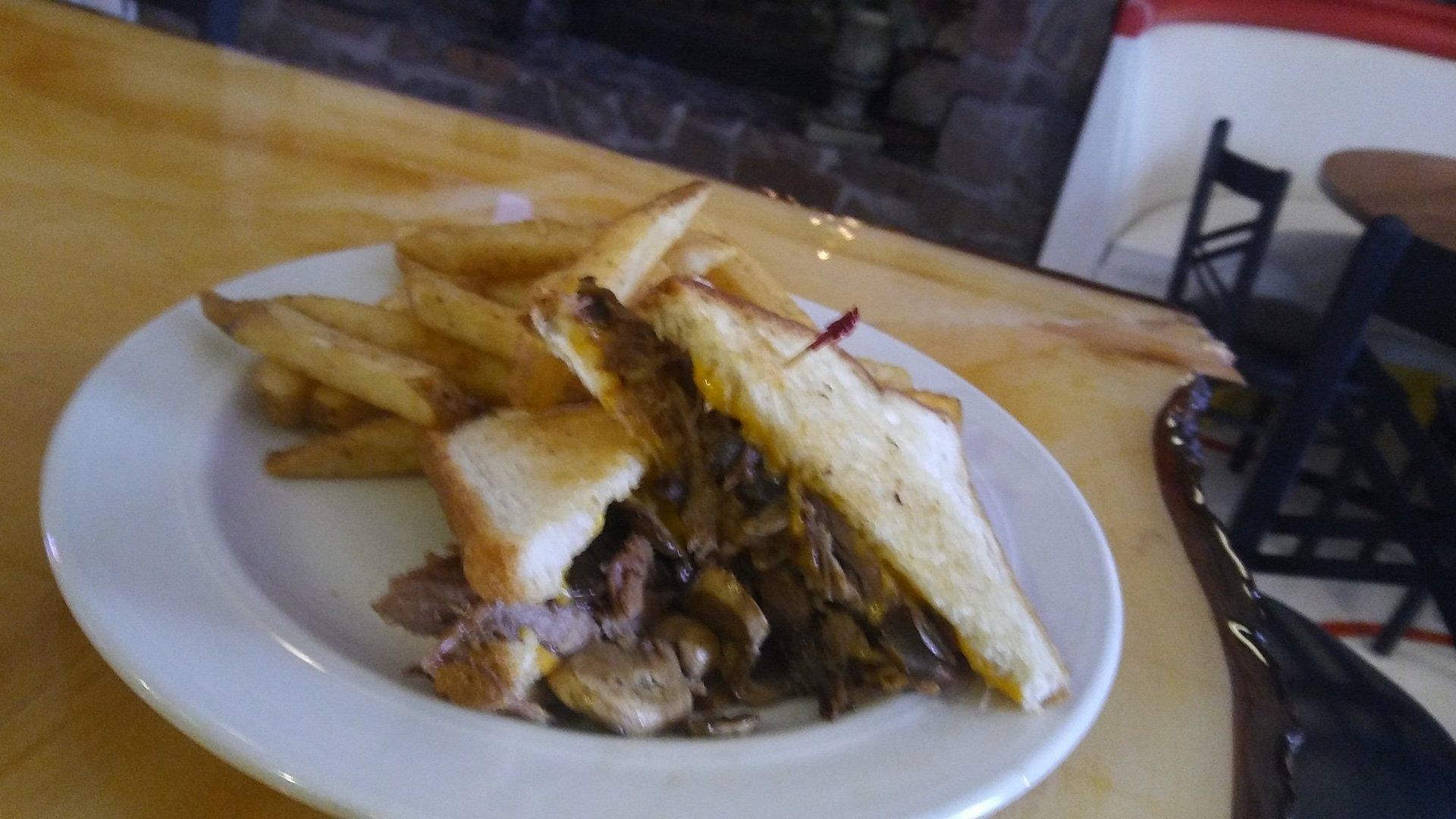 Sandwich and fries on a white plate on a wooden table in a café