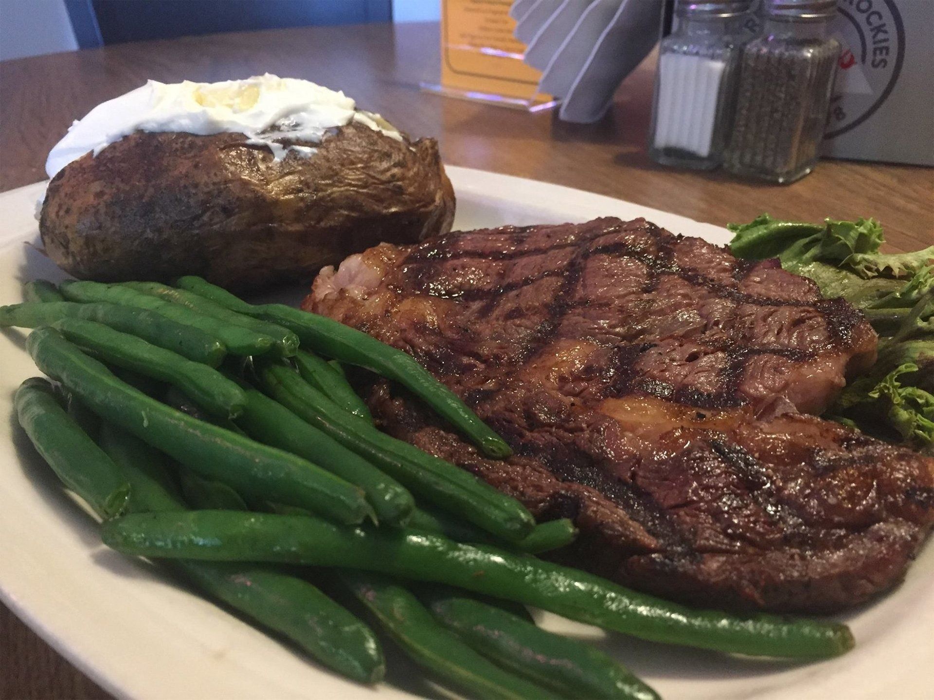 Grilled steak, green beans, and baked potato on a dinner plate at a restaurant table