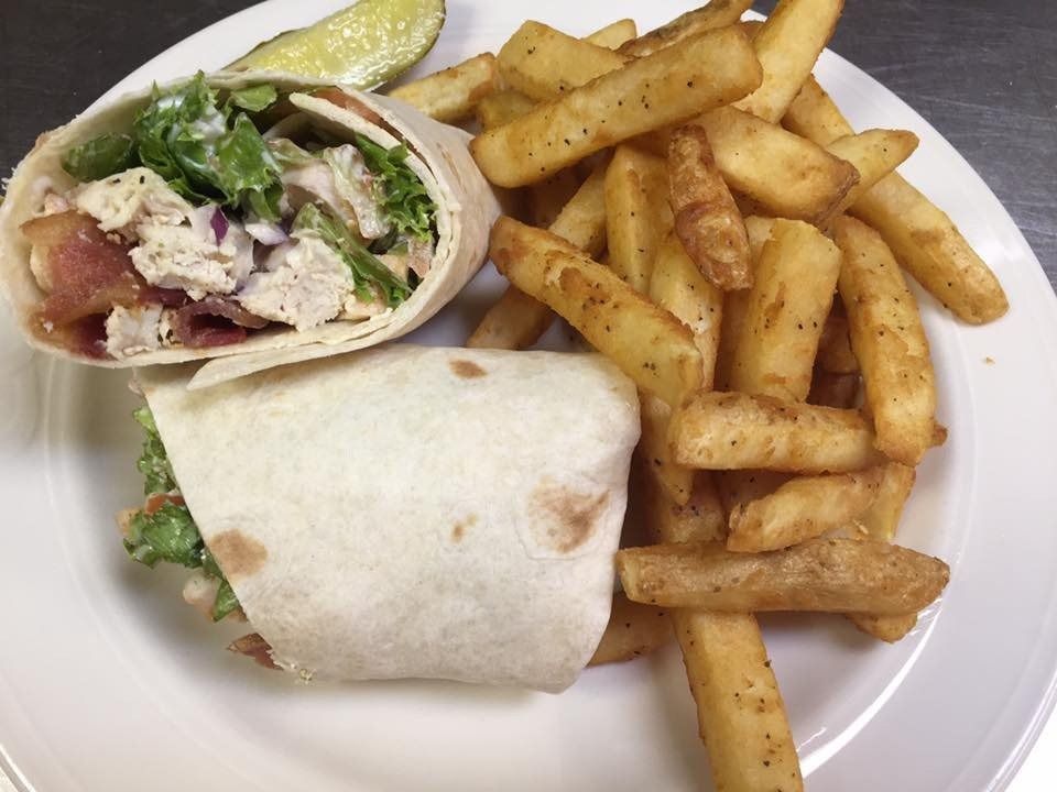 Wrap sandwich and seasoned fries on a white plate, with a pickle slice on the side.