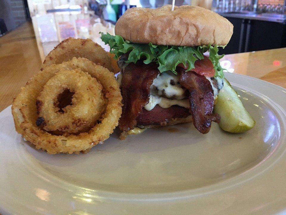 Burger with onion rings and a pickle on a white plate in a restaurant setting