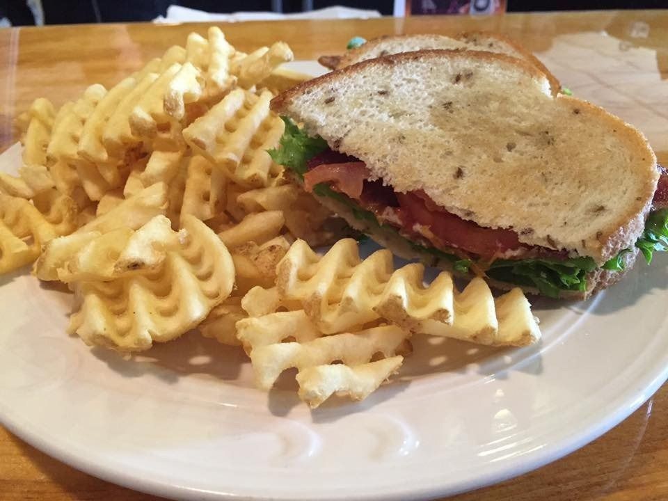 Sandwich on a white plate with waffle fries on the side