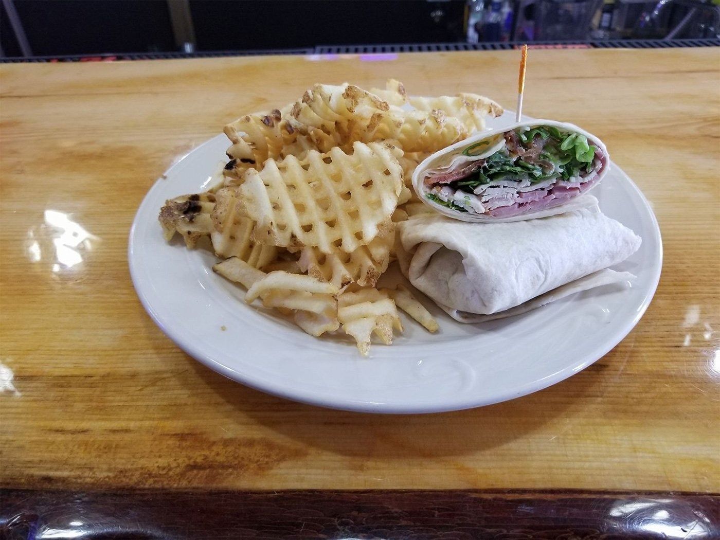 White plate with waffle fries and a wrap sandwich on a wooden table.