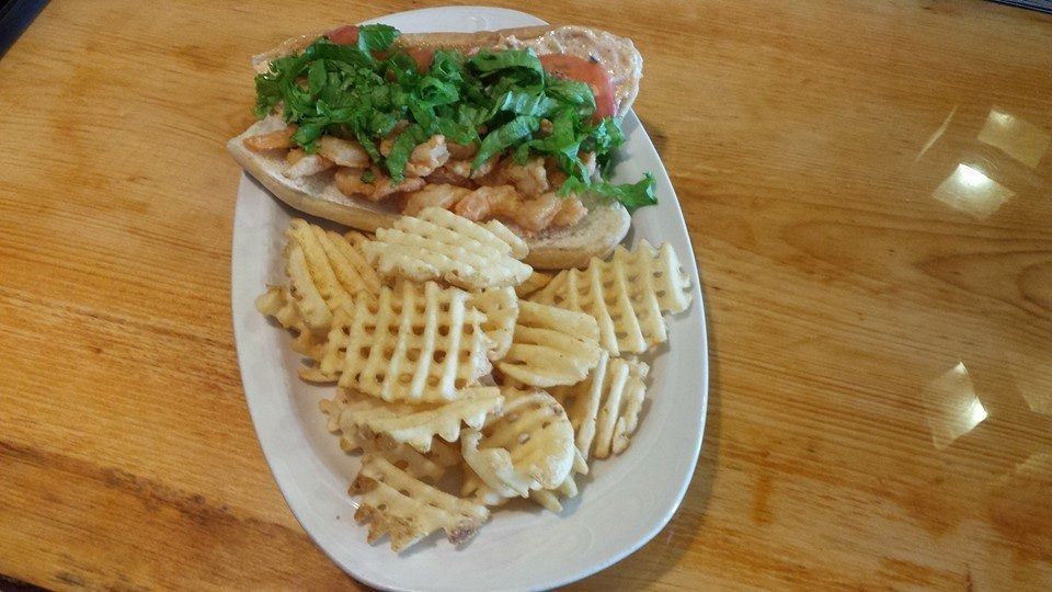Plated meal with waffle fries, sliced tomatoes, greens, and a sandwich on a wooden table