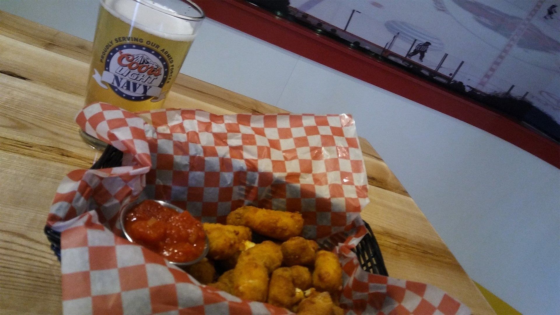 Basket of fried appetizers with red dipping sauce on a table beside a beer cup