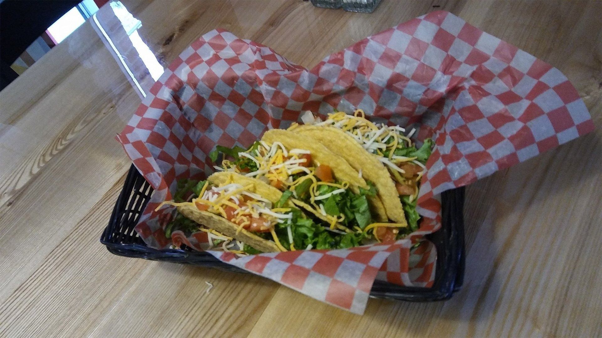 Taco salad in a black basket, lined with red-and-white paper, on a wooden table.