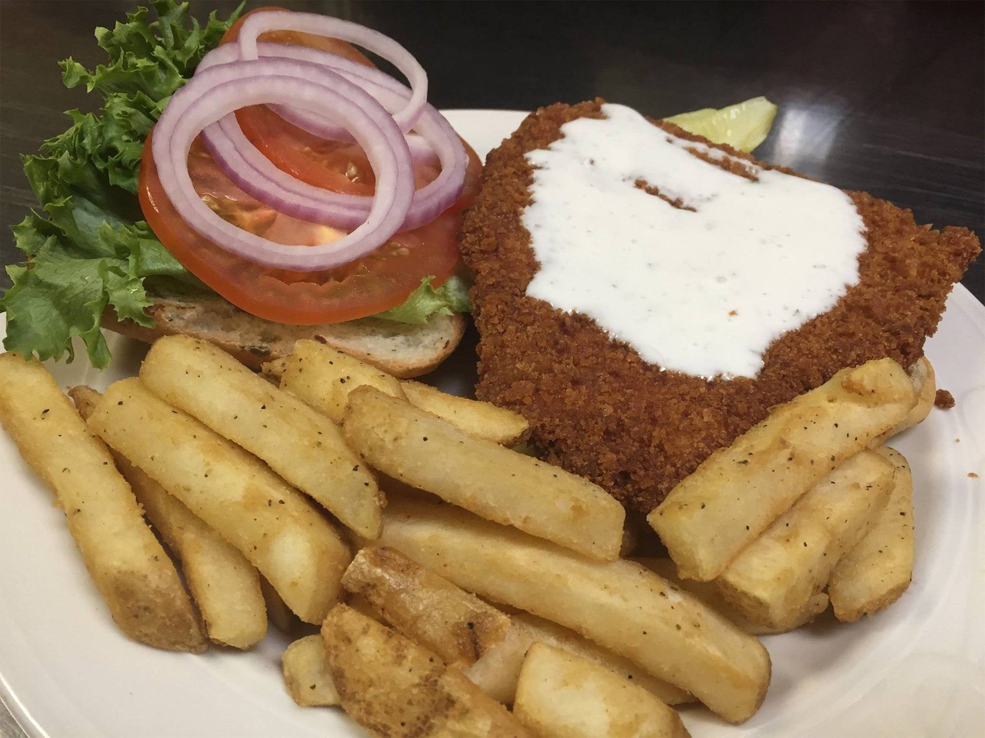 Breaded schnitzel with white sauce, fries, and a tomato-onion garnish on a plate