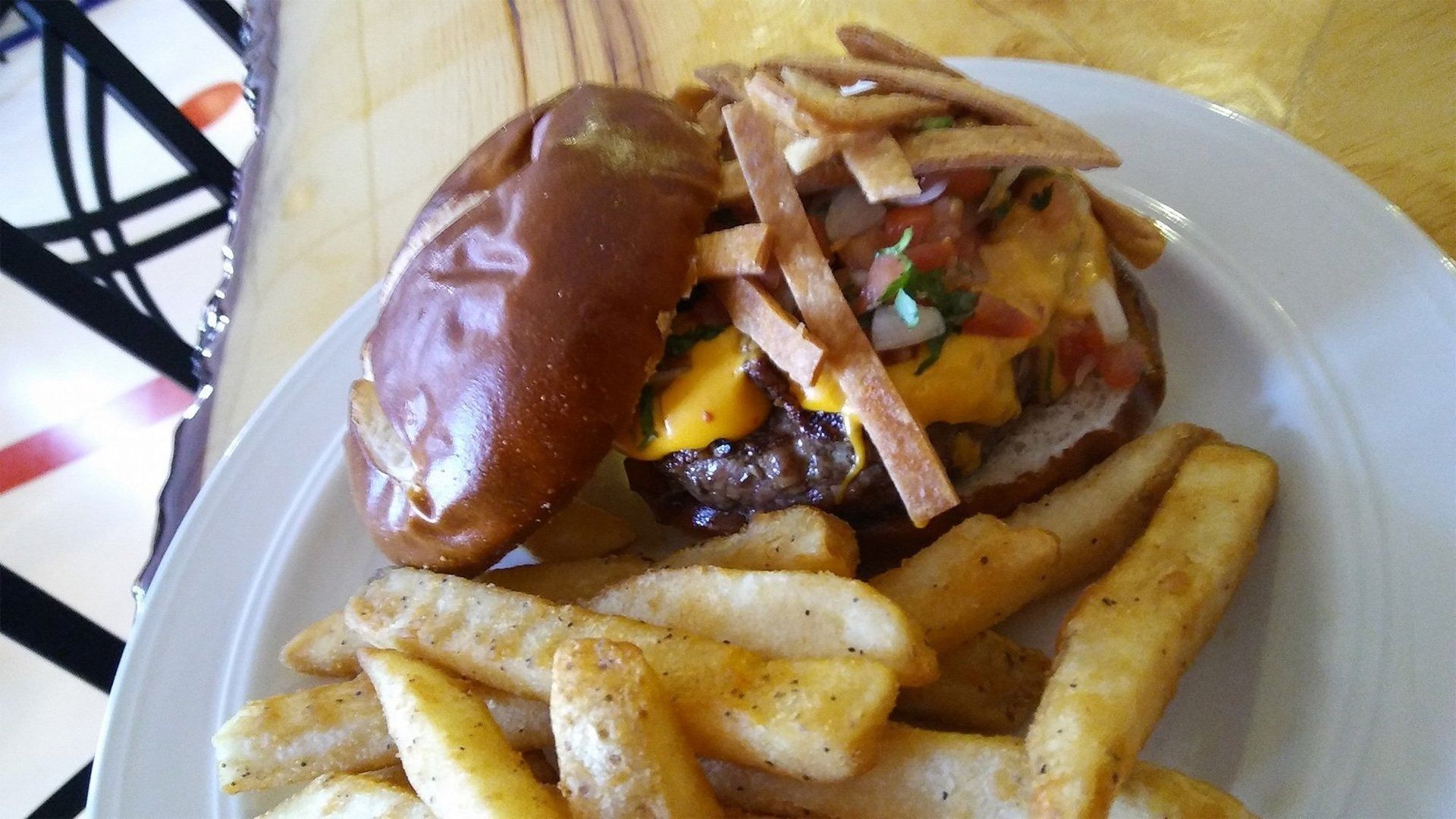 Burger topped with fries on a white plate with potato wedges on the side