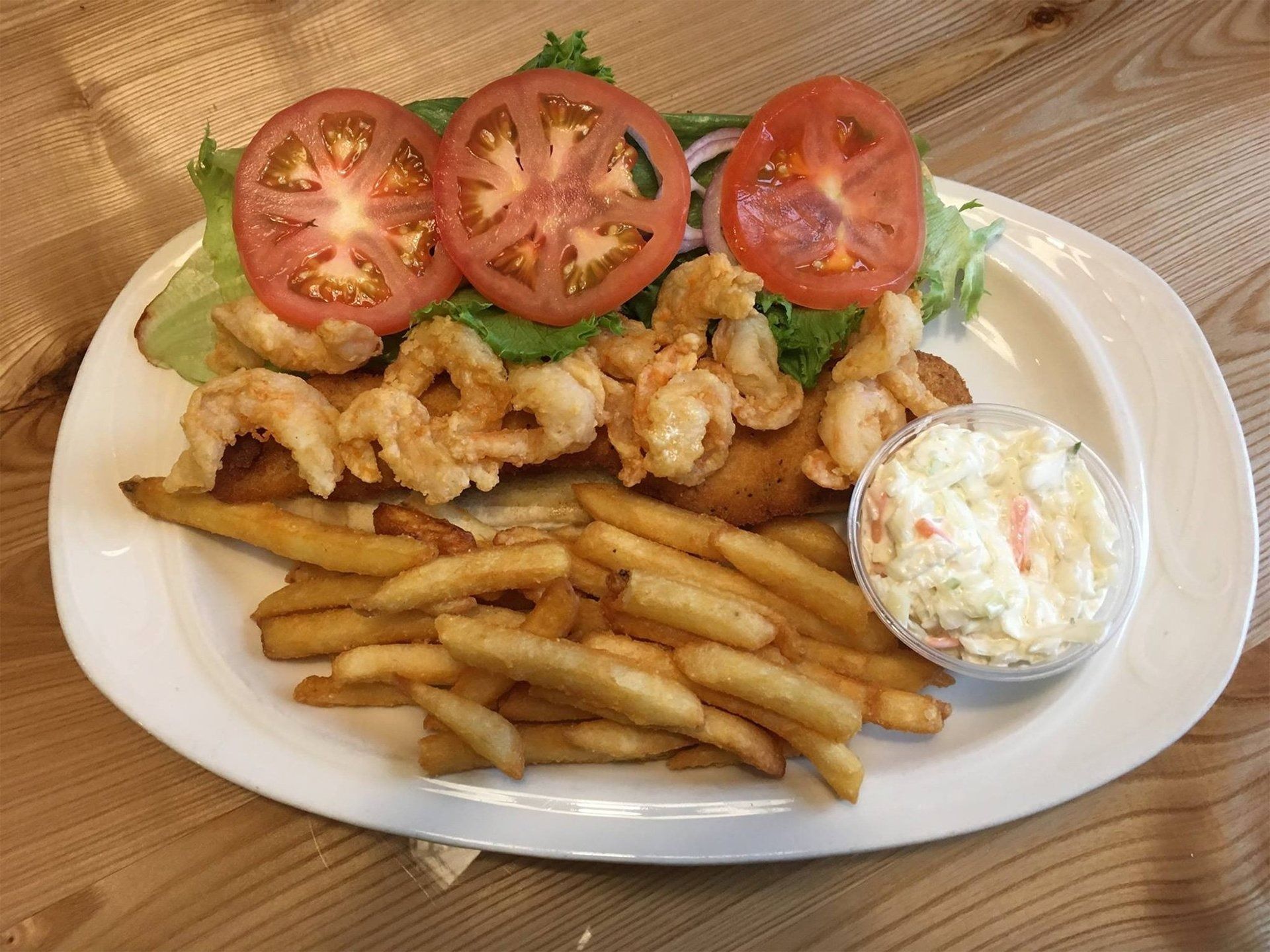 Plated fried sandwich with tomato slices, fries, and coleslaw on a white plate