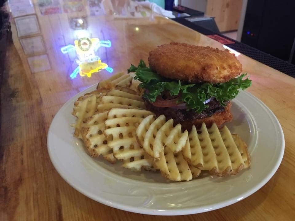 Waffle sandwich with greens on a plate beside waffle fries on a wooden table