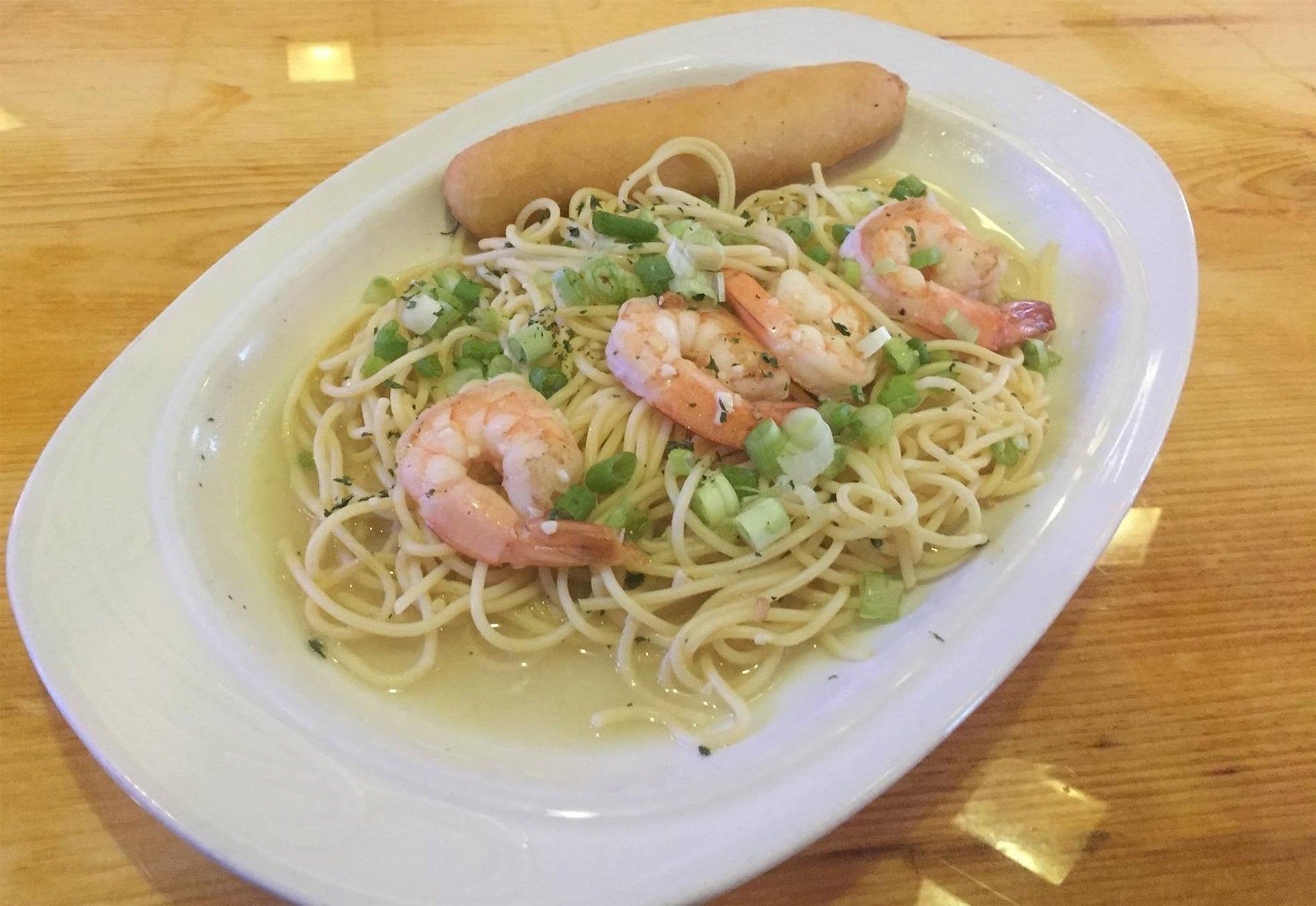 Shrimp spaghetti on a white oval plate with a breadstick on a wooden table