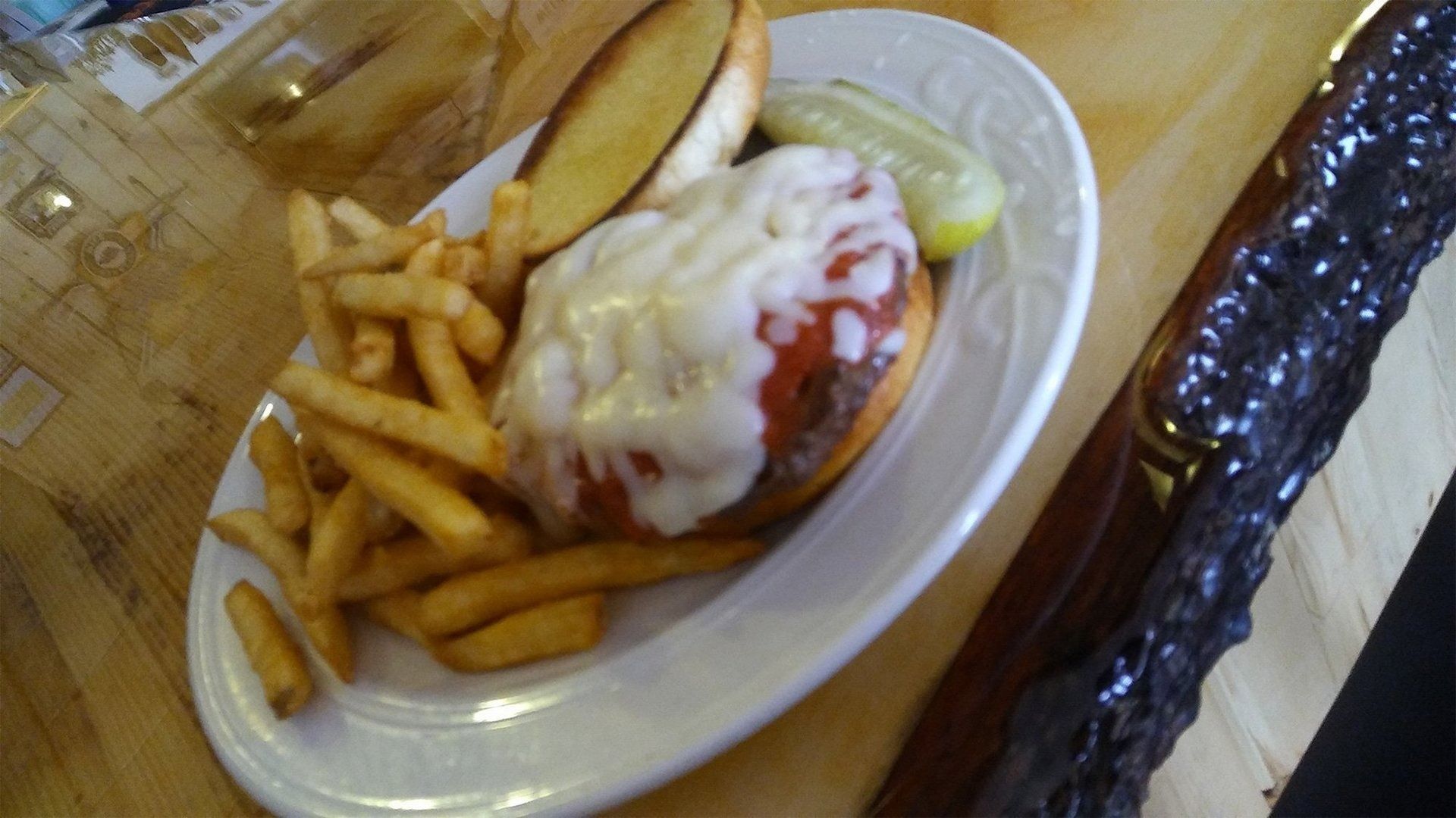 Burger and fries on a white plate with a pickle and ketchup on a wooden table.