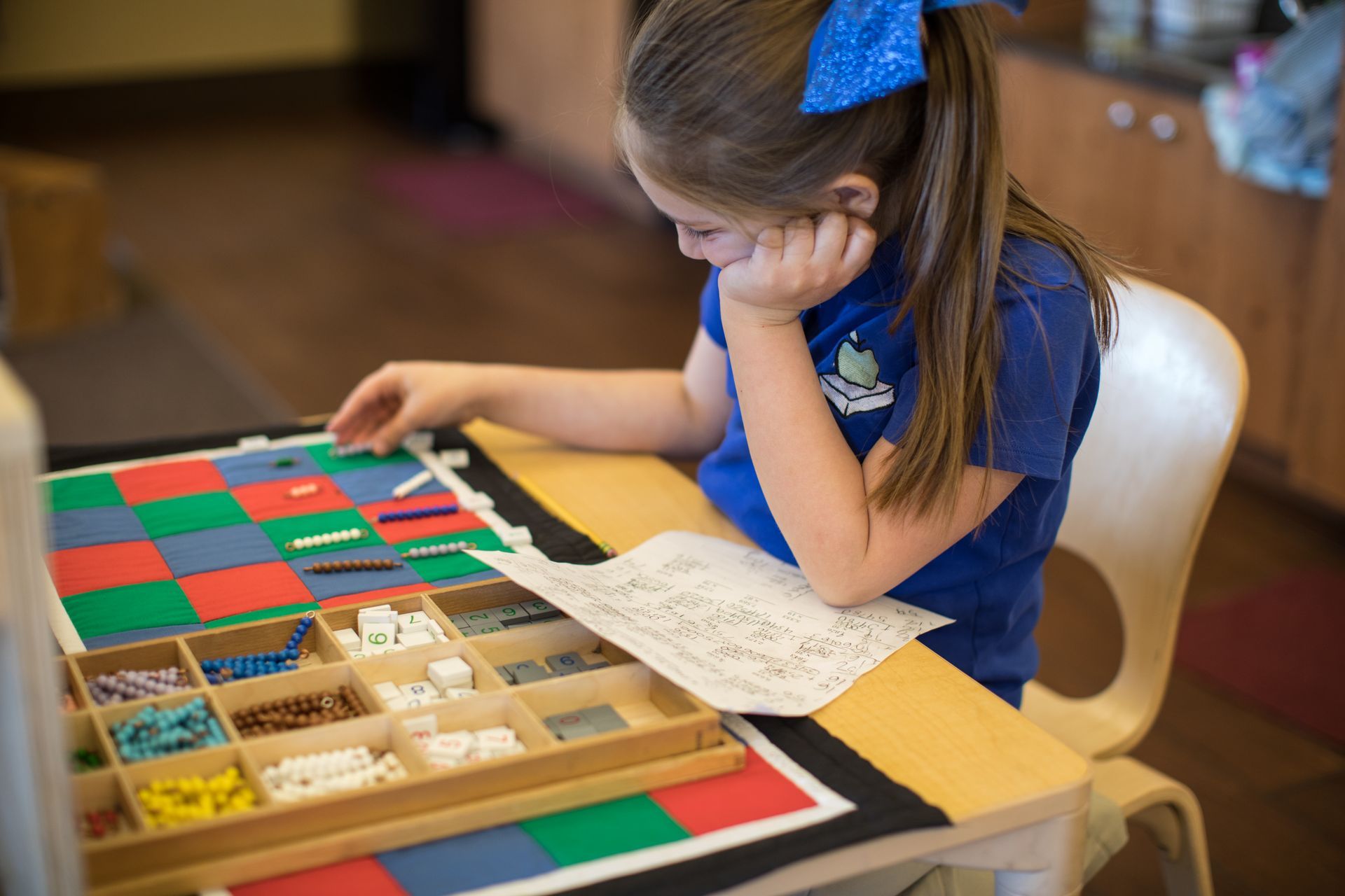 Child in blue shirt studying a color sorting board with trays of small objects at a table