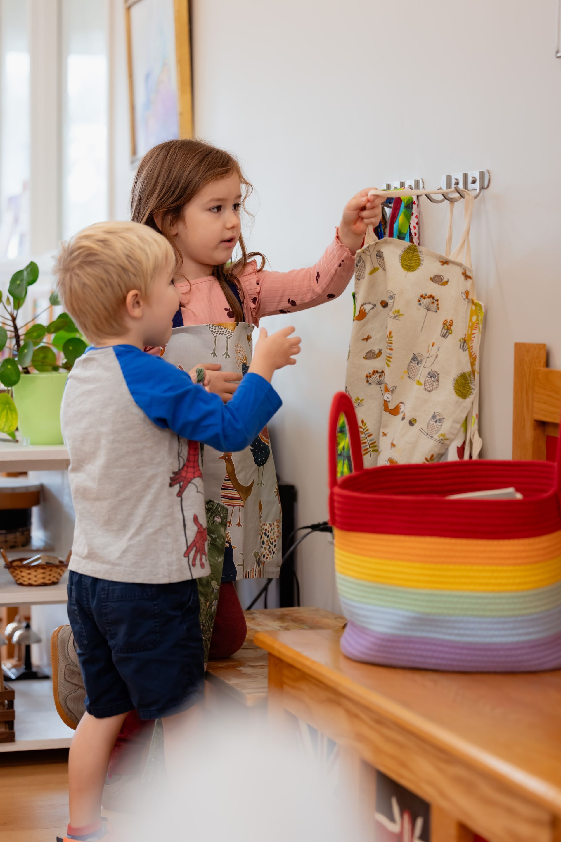 A child helping another beside a colorful striped basket indoors
