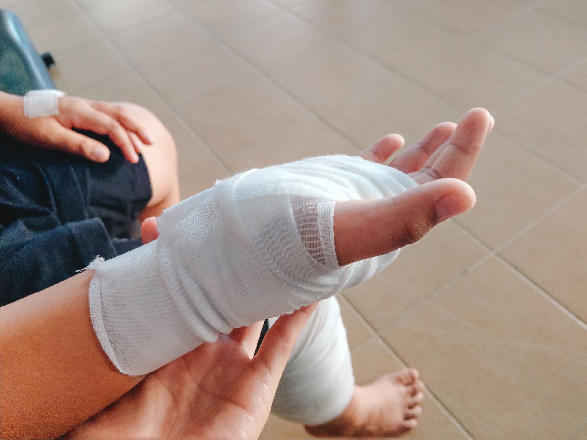 Bandaged foot and lower leg being supported by hands indoors on a tiled floor
