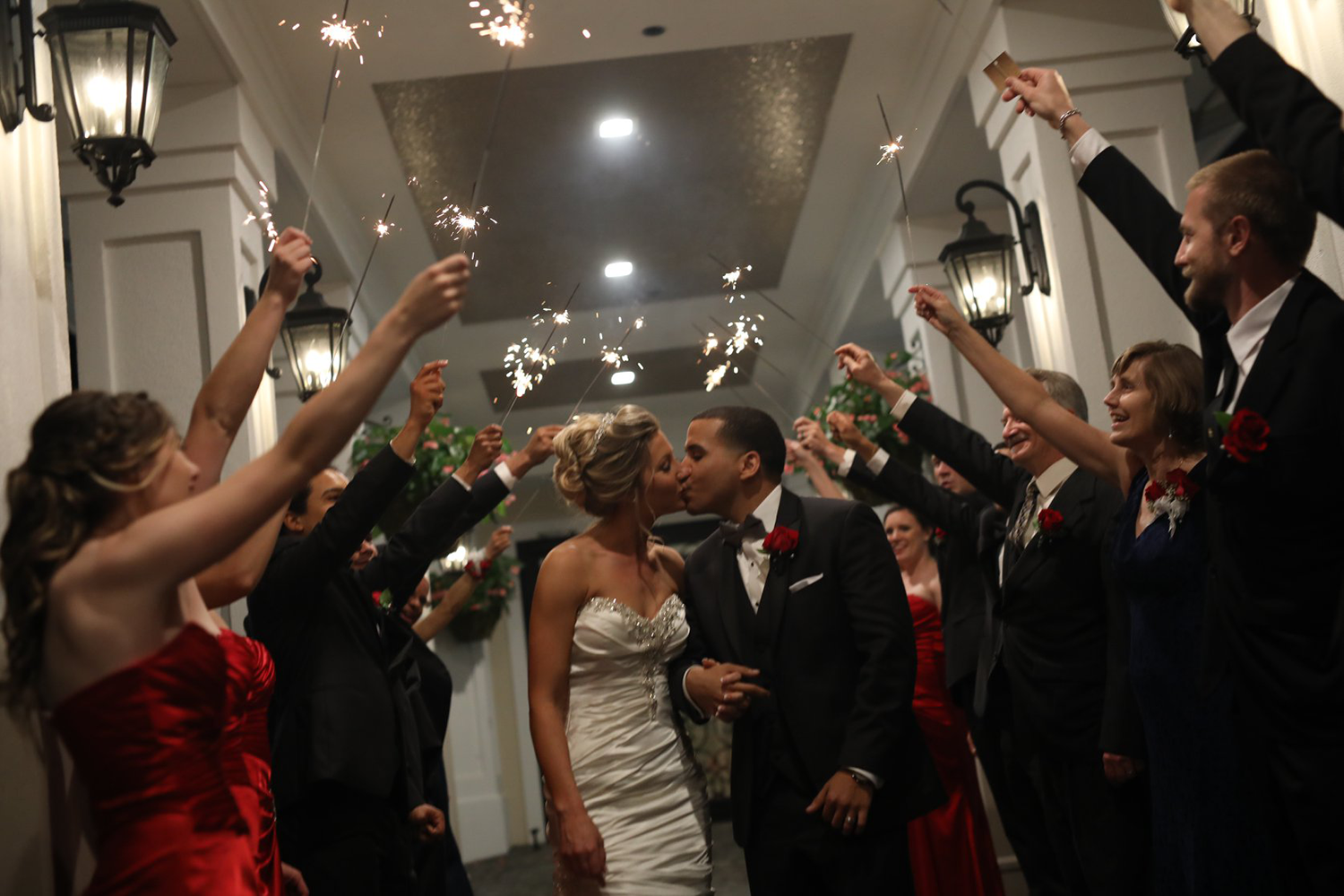 A bride and groom are kissing while their wedding party holds sparklers in the air.