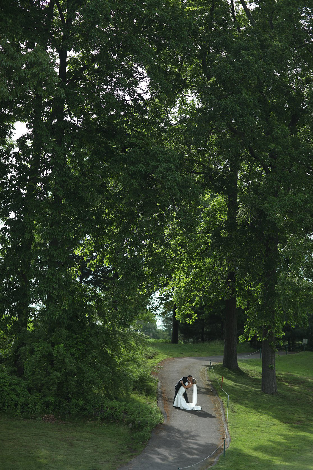 A bride and groom are kissing on a path in the woods