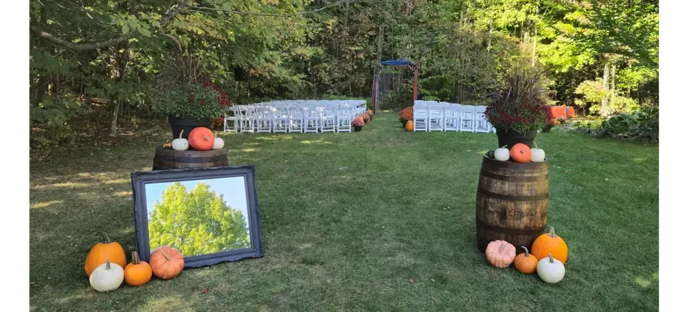 A wedding ceremony is being held in a field decorated with pumpkins and barrels.