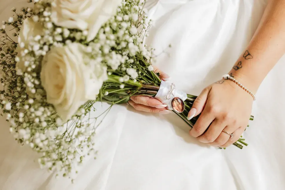 A bride in a white dress is holding a bouquet of white roses and baby 's breath.