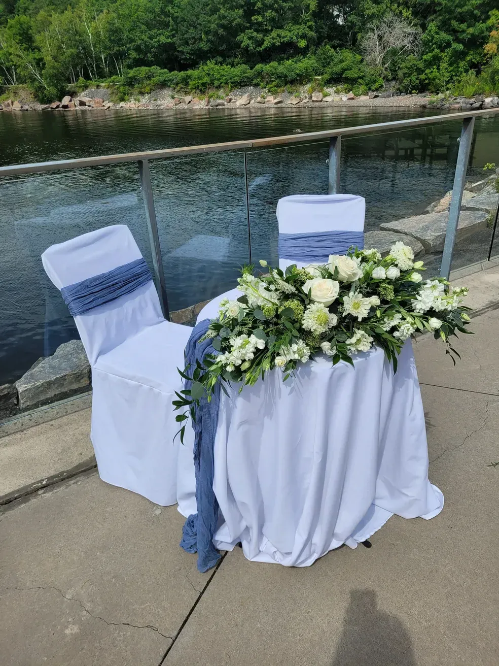 A table with two chairs and flowers on it in front of a body of water.