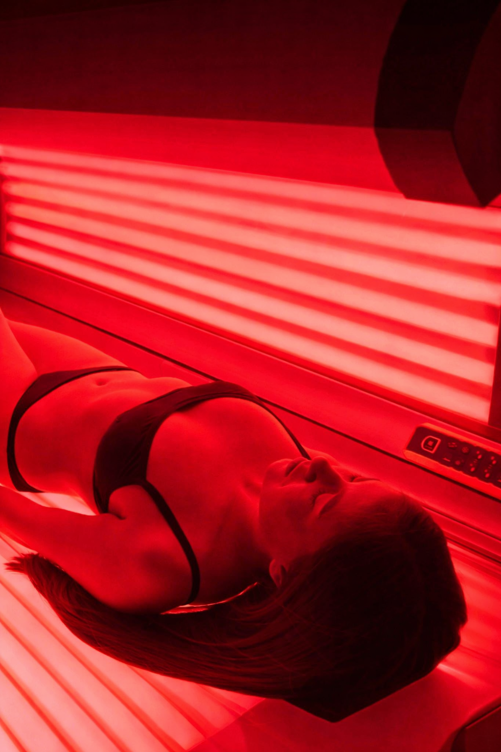 Person lying in a red-lit tanning bed with the lid open