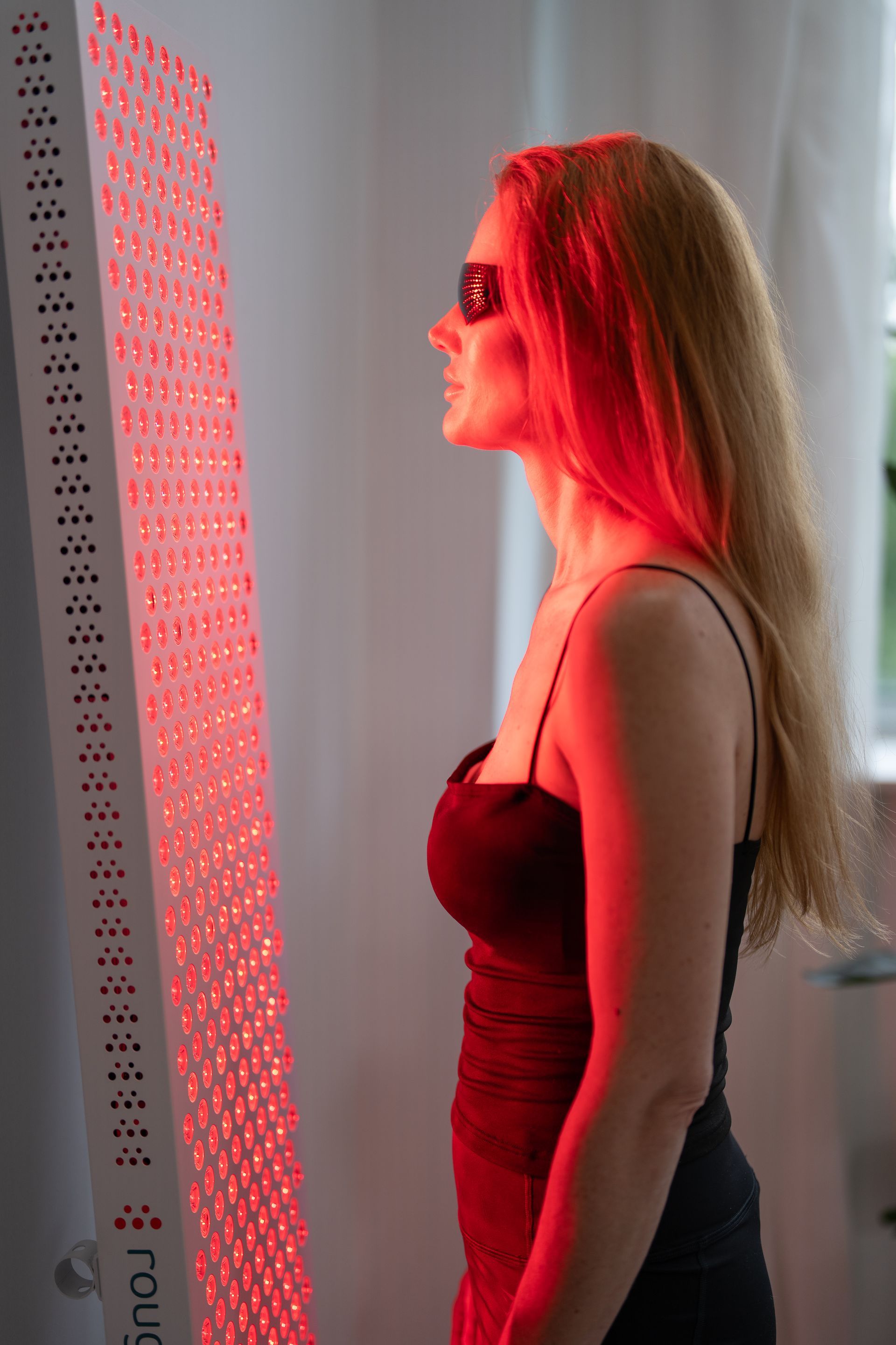 Woman in red light glasses facing a glowing red panel indoors