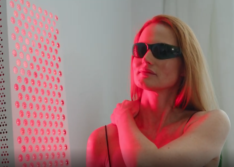 Woman in sunglasses lit by red light beside a glowing red panel