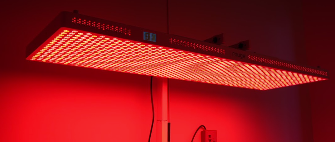Red LED grow light panel glowing over hanging cables against a red wall